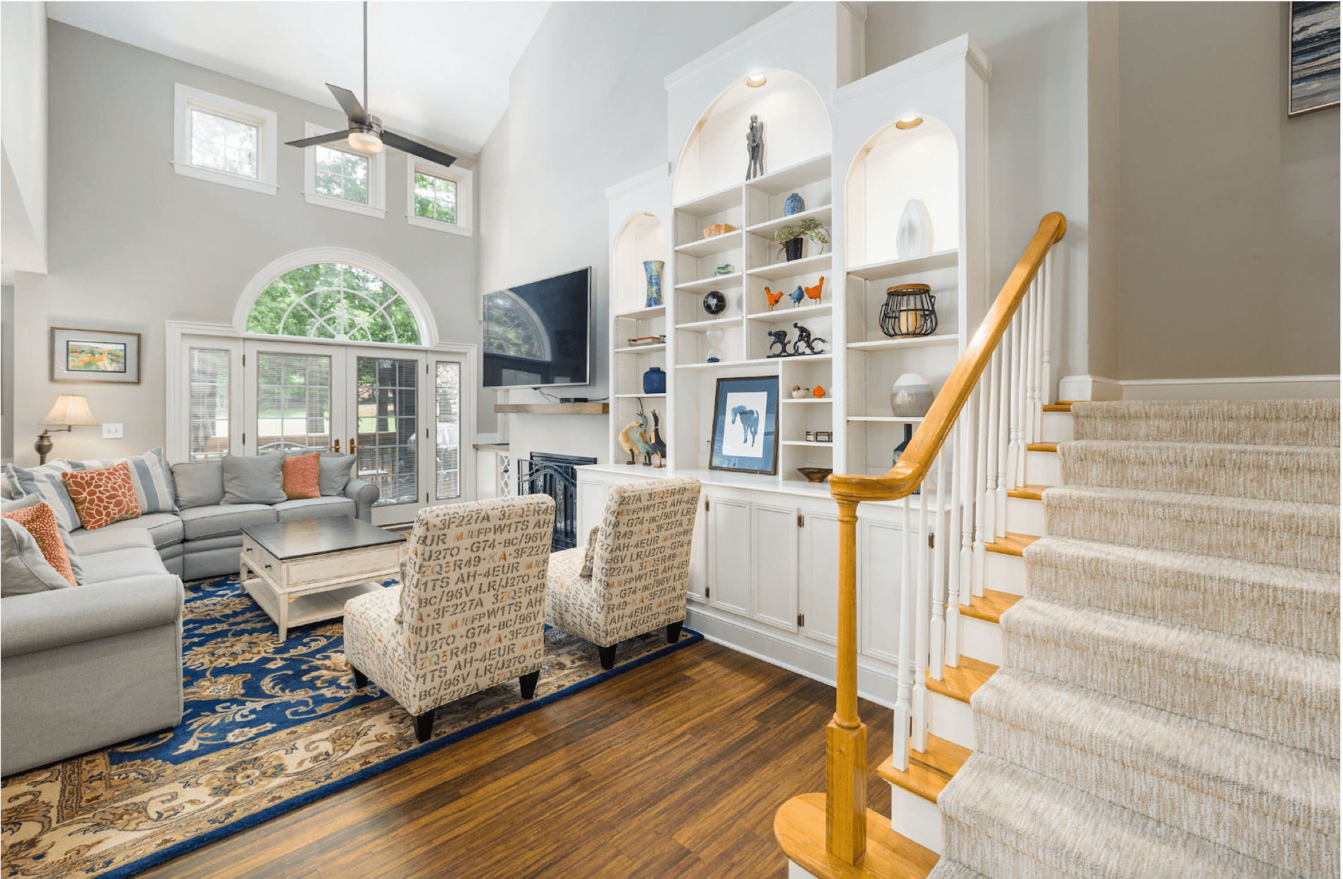 large living room with wood paneled floors, a intricately detailed blue and gold rug, high ceilings, and a color scheme of beiges and white